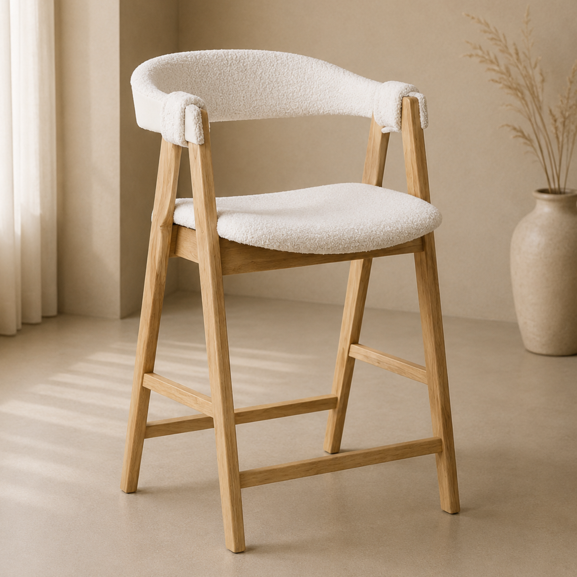 A modern wooden bar stool with a cream bouclé upholstered seat and curved backrest, set in a minimalist beige room with a vase of dried grass in the background.