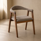 A modern wooden dining chair with a curved upholstered backrest and seat cushion, shown in a minimalist beige room with soft natural light.