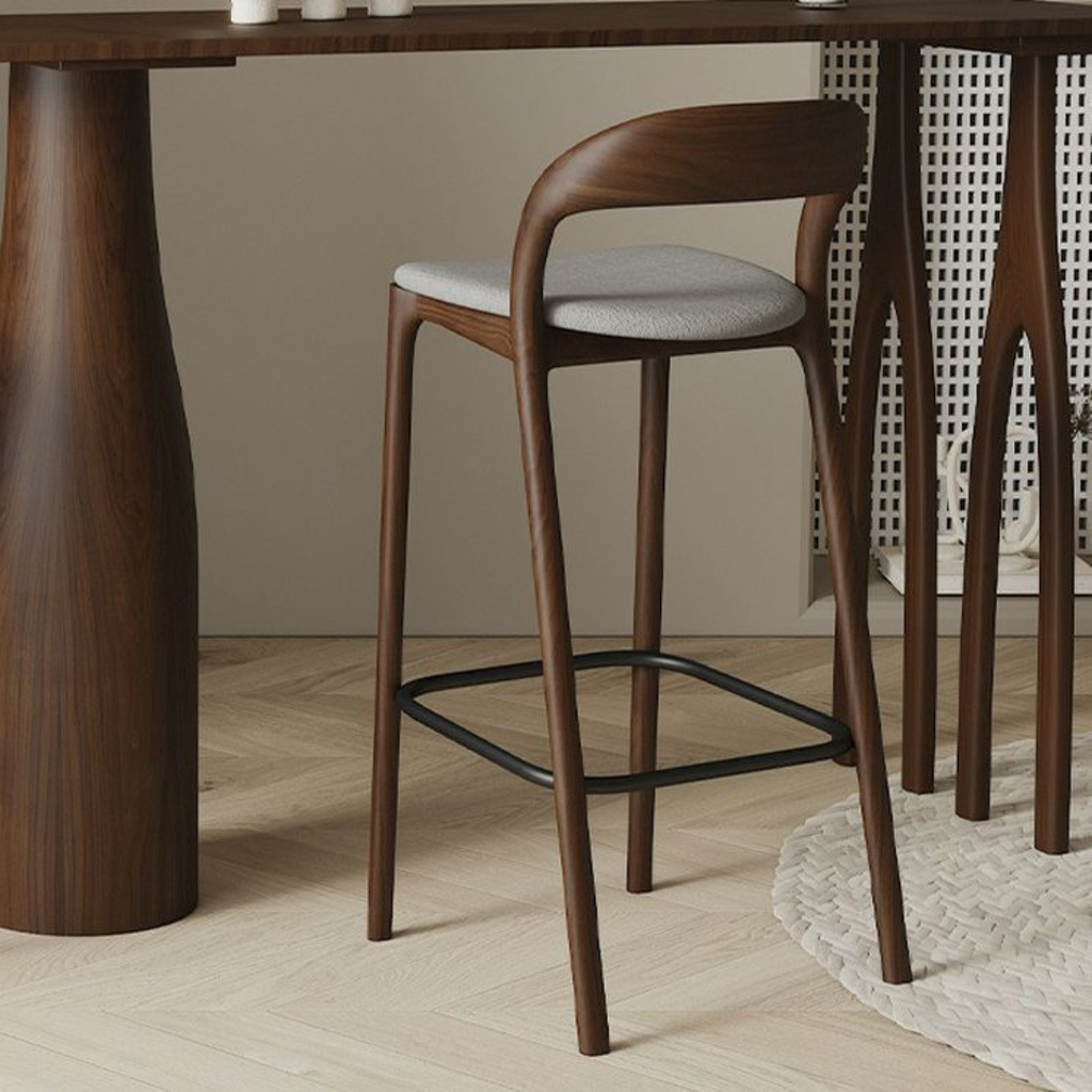 Wooden bar stool with a gray cushion next to a wooden table.