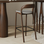 Wooden bar stool with a gray cushion next to a wooden table.