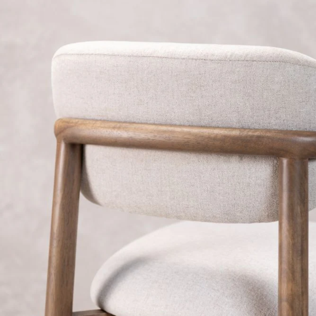 Close-up of a bar stool with wooden frame and cream cushioned seat and backrest on a light background