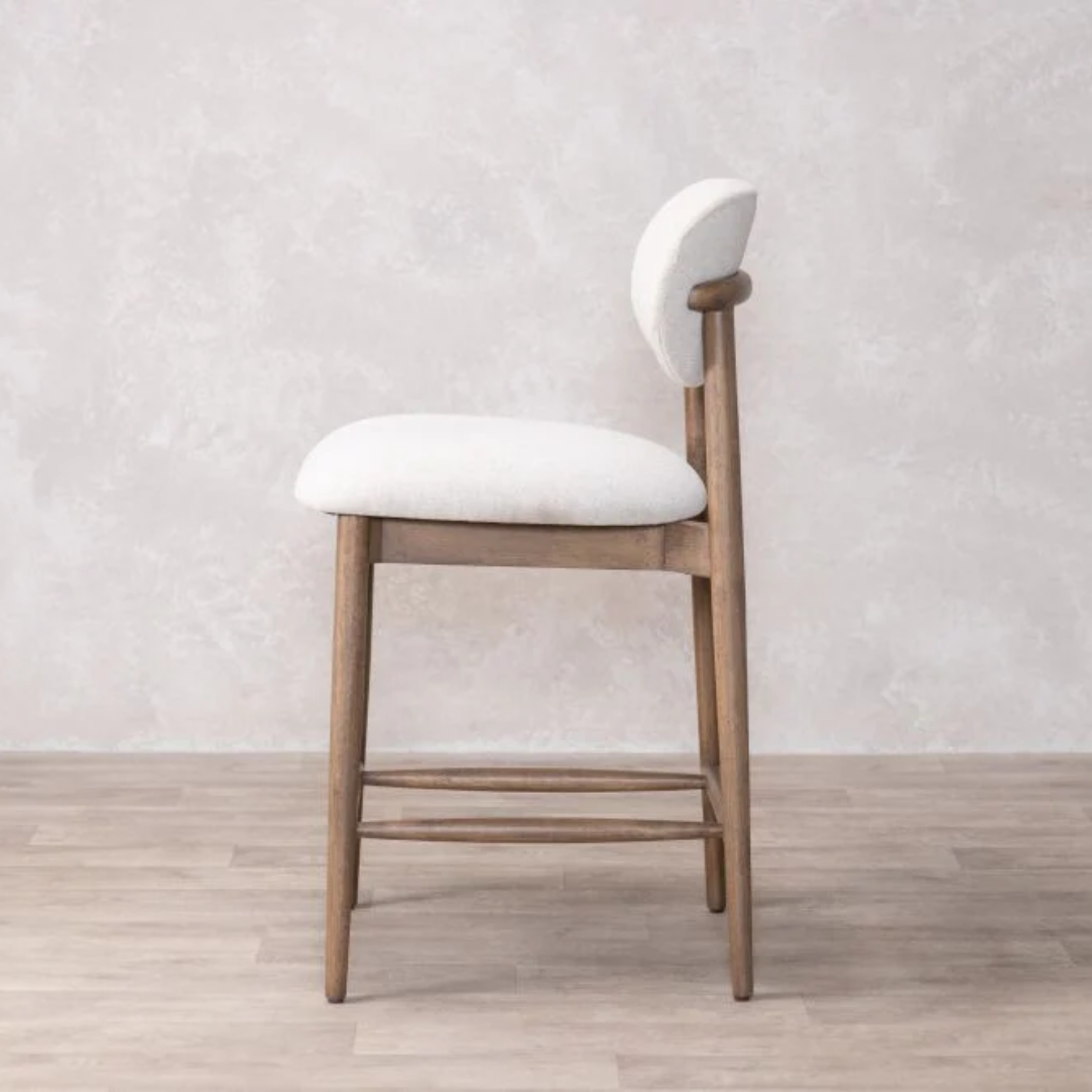 Wooden bar stool with cream  cushioned seat and backrest on a light wooden floor.