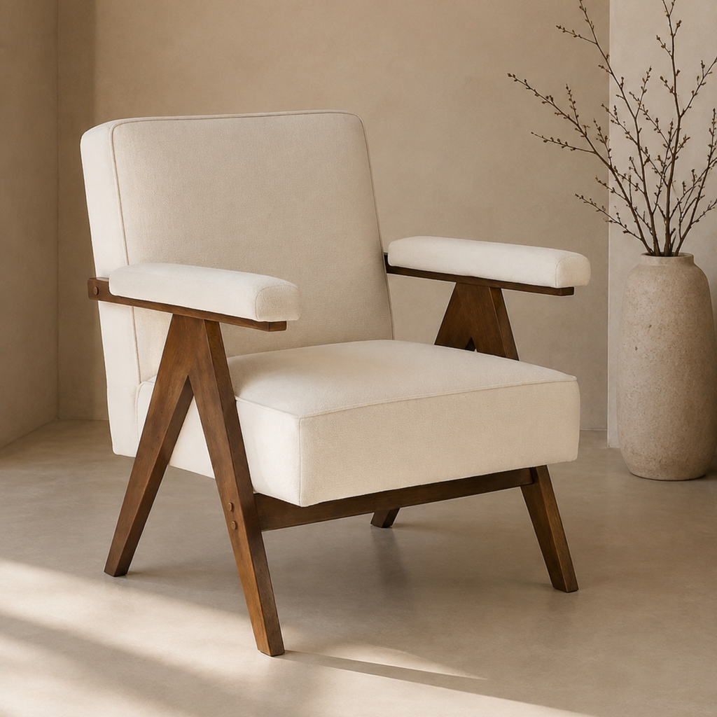 A modern accent chair with cream-colored upholstered cushions and a dark brown wooden frame, set in a minimalist room with a beige wall and floor, next to a large textured vase with dried branches.
