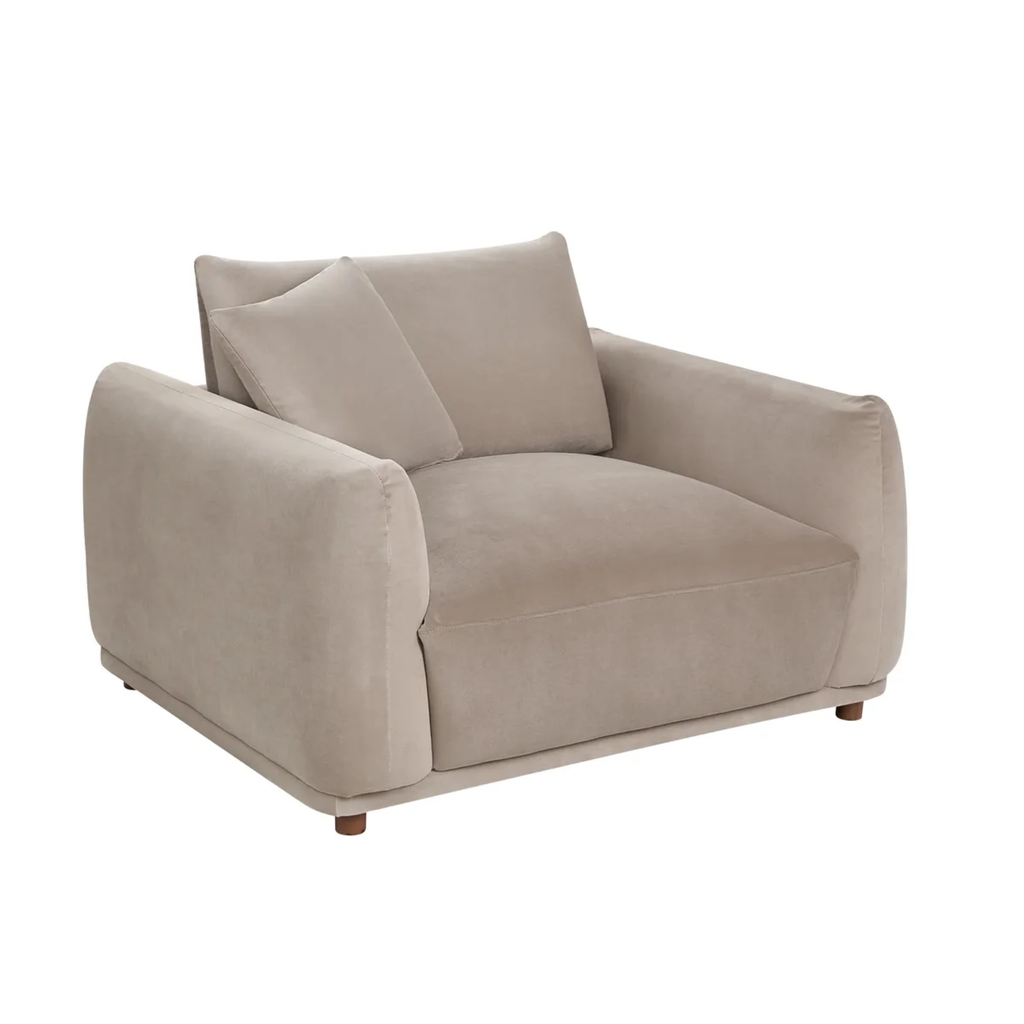 A modern low-profile armchair upholstered in a soft, light taupe-beige velvet fabric, featuring two matching back cushions and small dark wooden legs, shown against a plain white background.