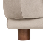 Close-up of a beige upholstered furniture piece showing the fabric texture, stitched seam, and a dark brown cylindrical wooden leg on a white background.