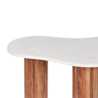 A close-up of a modern table with a wavy, organic-shaped white marble top and two round wooden legs with vertical grain.