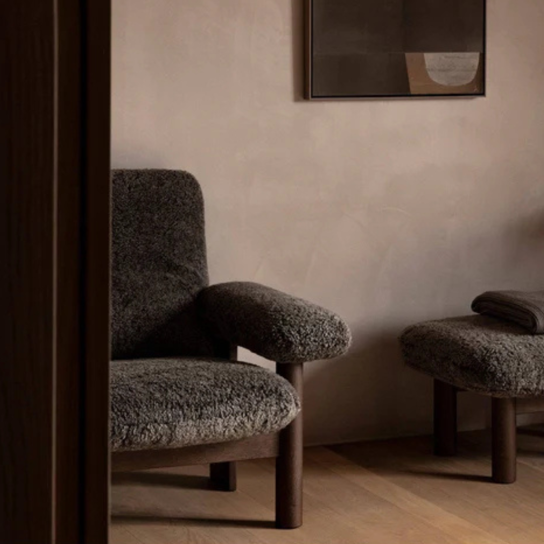 Dark textured armchair and stool against a beige wall with abstract art.