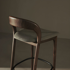 Bar stool with wooden frame and green cushioned seat against a dark background