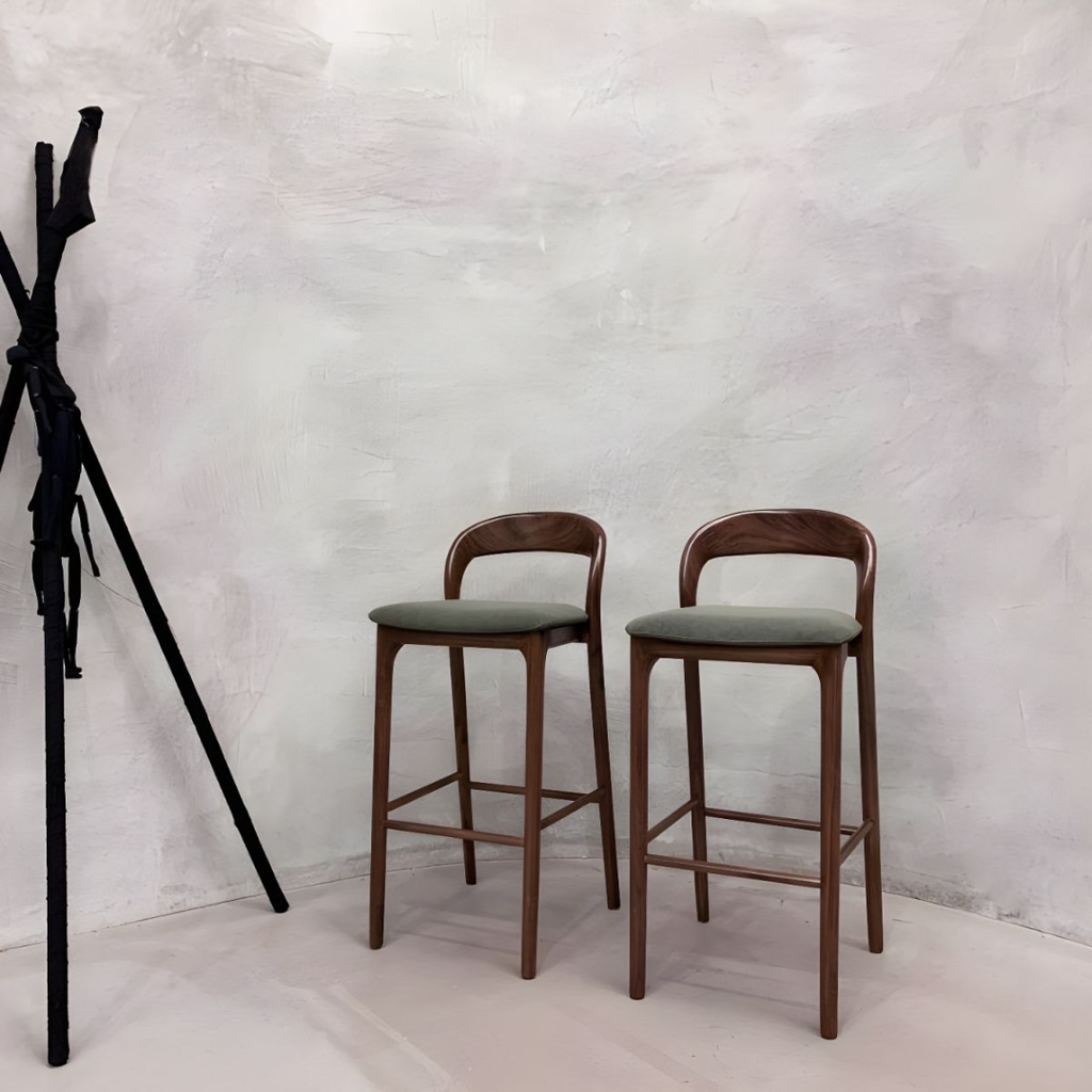 Two wooden bar stools with green seats against a textured white wall.