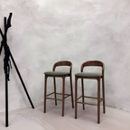Two wooden bar stools with green seats against a textured white wall.