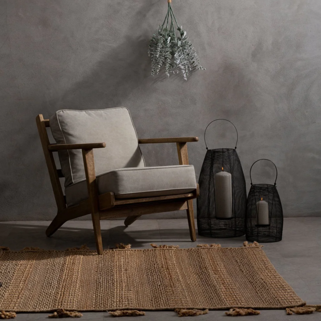 Wooden armchair with grey cushions next to dark lanterns on a textured rug.