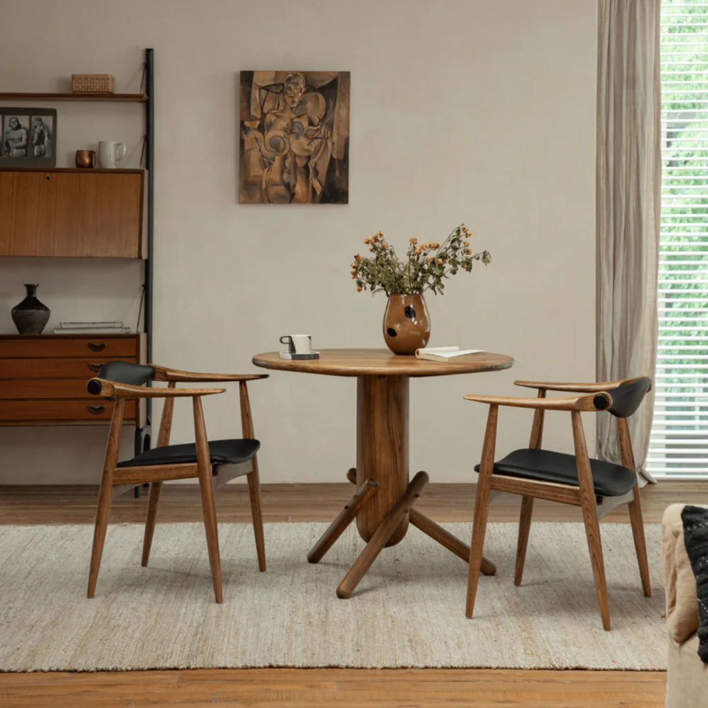 Dining room with wooden table and Wood And Black Leather Dining Chairs, with a vase with flowers, and wall art.