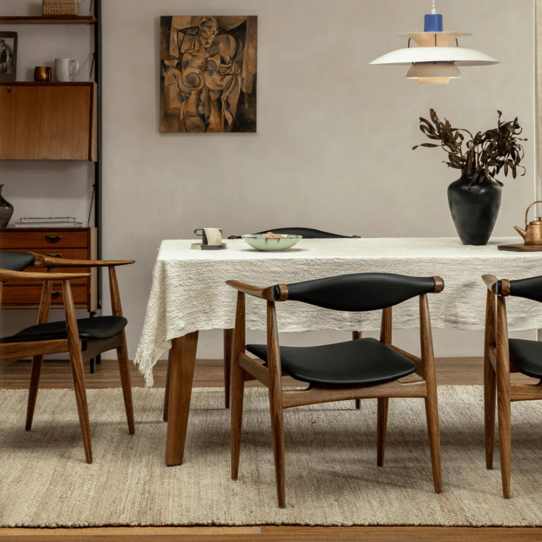 Dining room with wooden table and Wood And Black Leather Dining Chairs with a white tablecloth, and decorative elements.