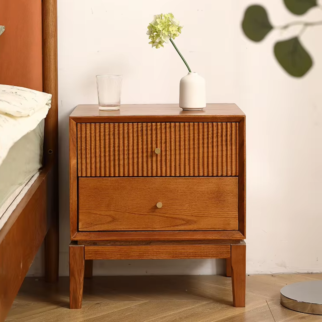 Retro Solid Wood Bedside Table With Two Drawers, a glass, and a vase with flowers on top, next to a bed.