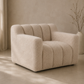 A modern boucle armchair in a warm beige color, styled in a minimalist room with a textured beige wall, a vase with dried branches, and soft sunlight casting shadows.