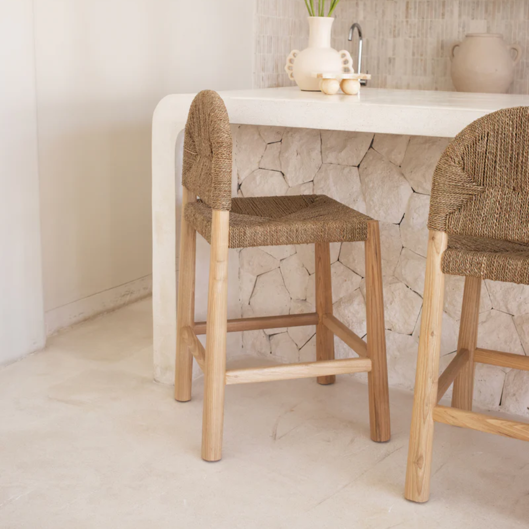 Two woven bar stools in front of a white countertop with decorative items.