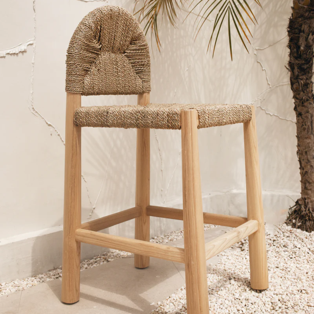 woven and Wooden bar Stool With Curved Back against a textured wall.