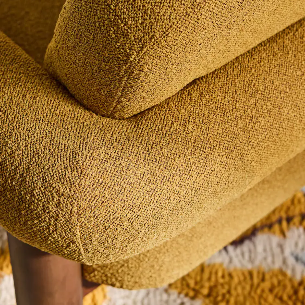 Close-up of a textured mustard yellow fabric with a blurred patterned background