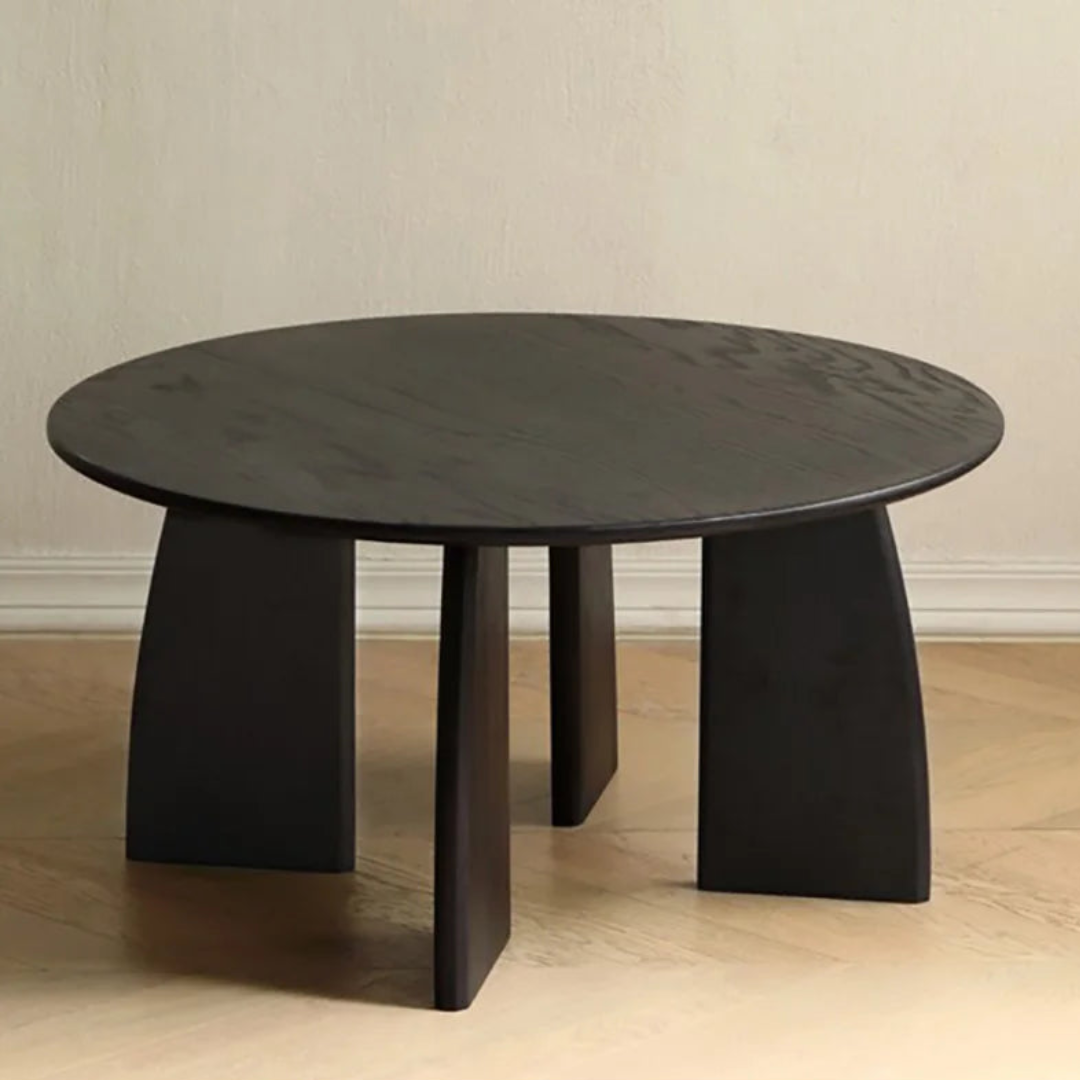 Black round table with three legs on a wooden floor against a beige wall.