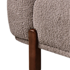Close-up of a textured bouclé upholstered chair or sofa in a warm taupe-beige color, showing the fabric texture and a dark brown wooden leg against a white background.
