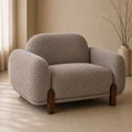 A modern low-profile armchair upholstered in a textured bouclé fabric in a warm taupe-beige color, with dark brown wooden legs, set in a minimalist beige room.