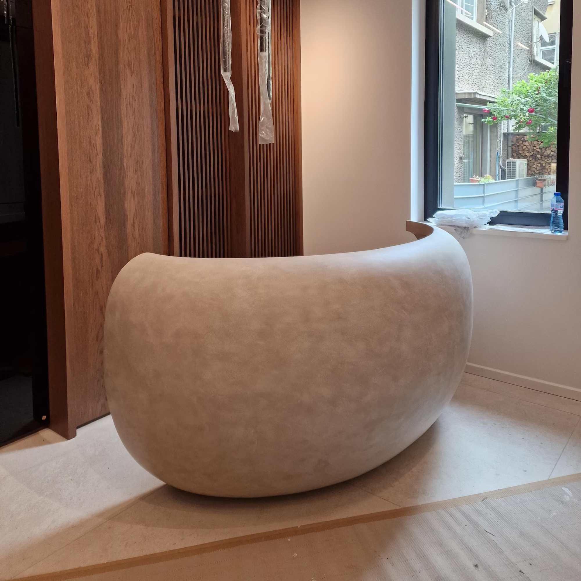 Beige stone Concrete Curved Reception Desk on a wooden floor with a window in the background