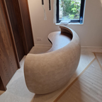 Modern, curved stone Concrete Reception Desk in a minimalistic room with wooden floor and window.