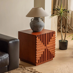 Wooden side table with geometric design, lamp, and plant in a living room setting.