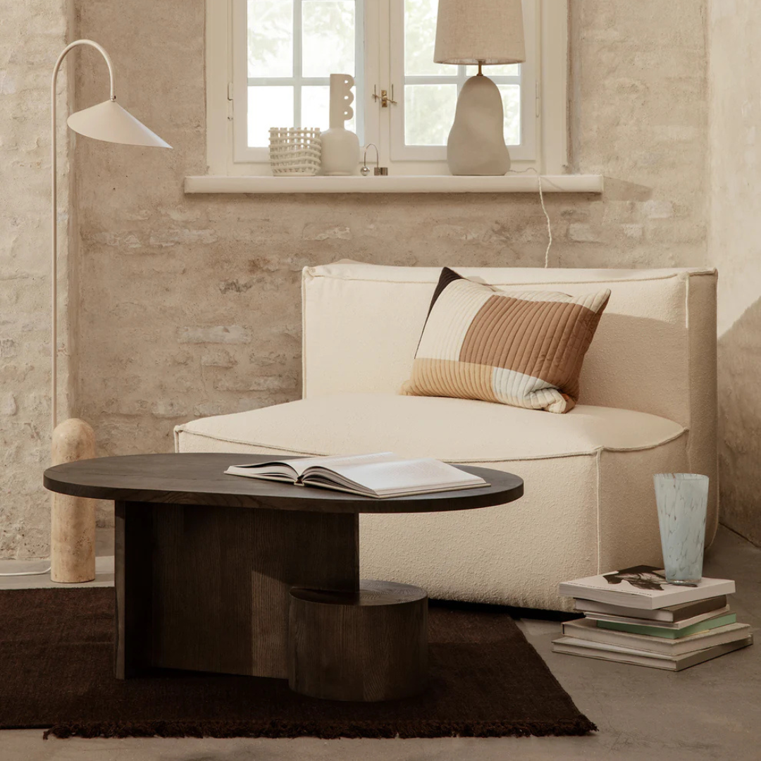 Beige sofa with a  Dark Wood Oval Coffee Table With Sculptural Base and decorative items in a modern living room.