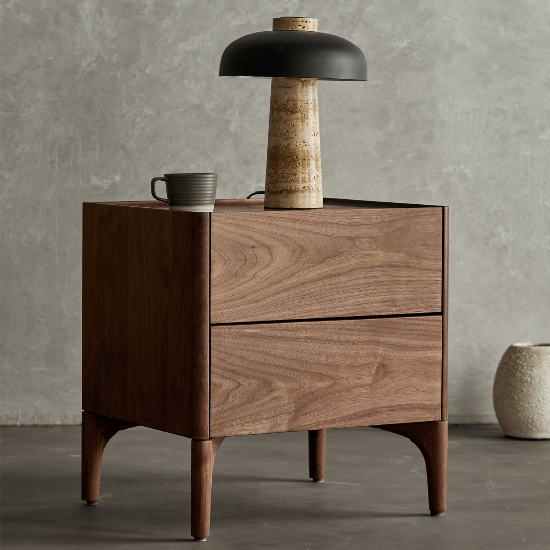 Walnut Bedside Table With Drawers With Curved Legs with a lamp and cup against a gray wall