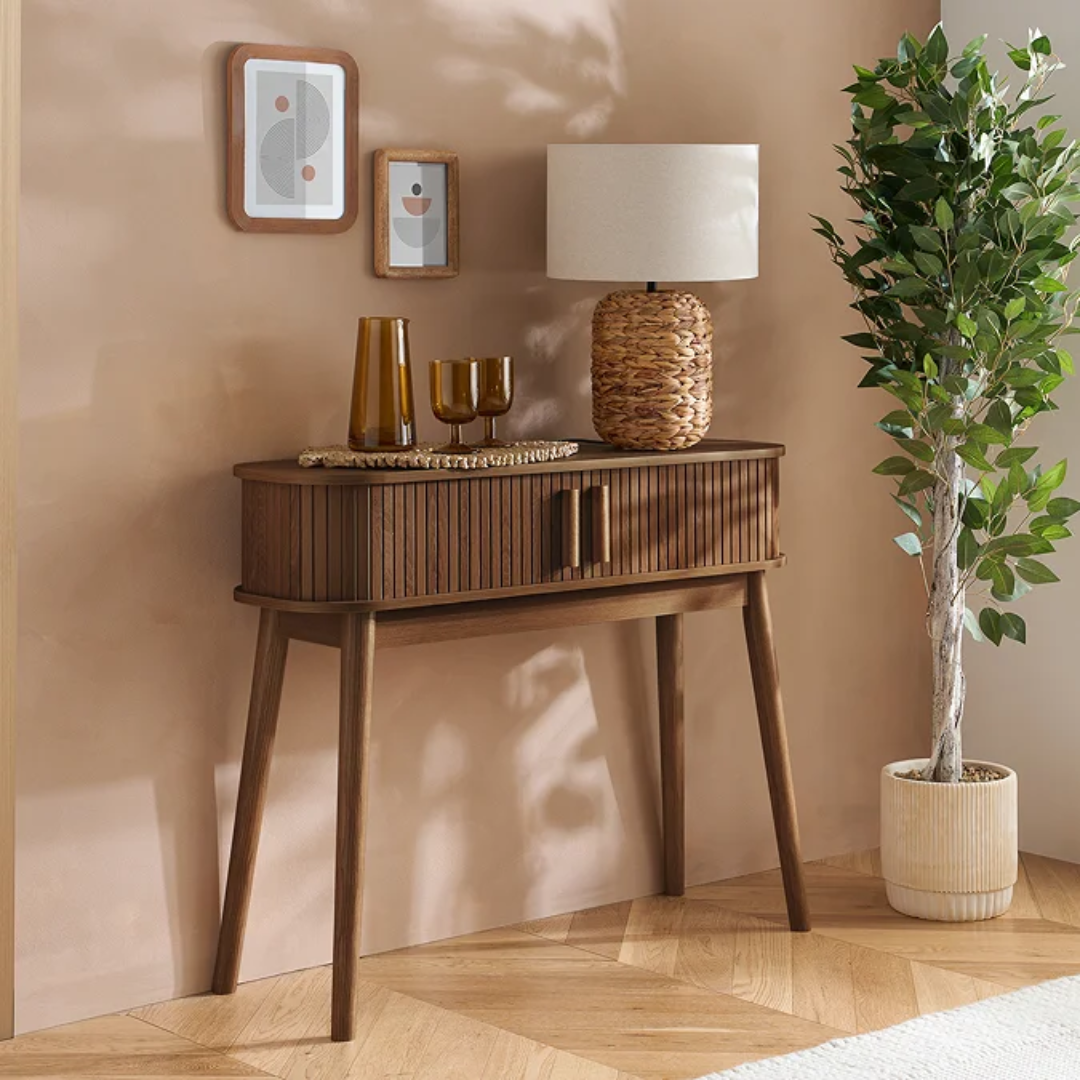 Walnut Narrow Fluted Console Table With Sliding Doors with decorative items against a beige wall.