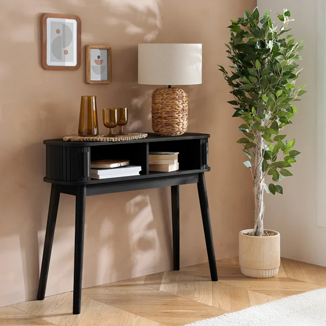 Modern Black Ribbed Console Table  with decorative items against a beige wall, featuring a lamp and plant.
